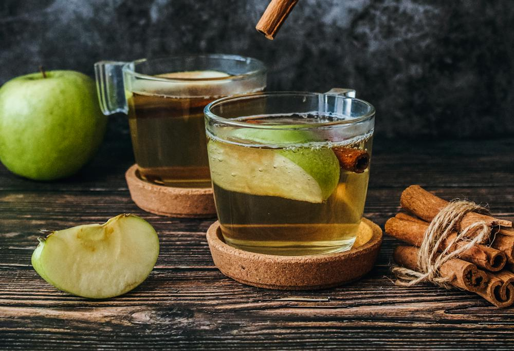 Sliced fresh apple and cinnamon sticks arranged on a wooden surface, prepared for making the SaunaCe Apple Cinnamon Soother drink.