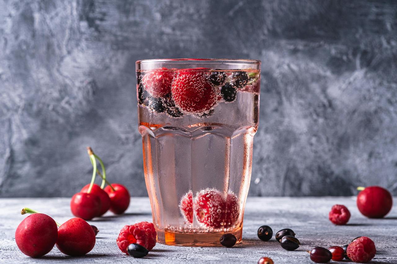 A glass filled with frozen cherries, mixed berries, and liquid ready to be blended for a cherry berry antioxidant blast smoothie.