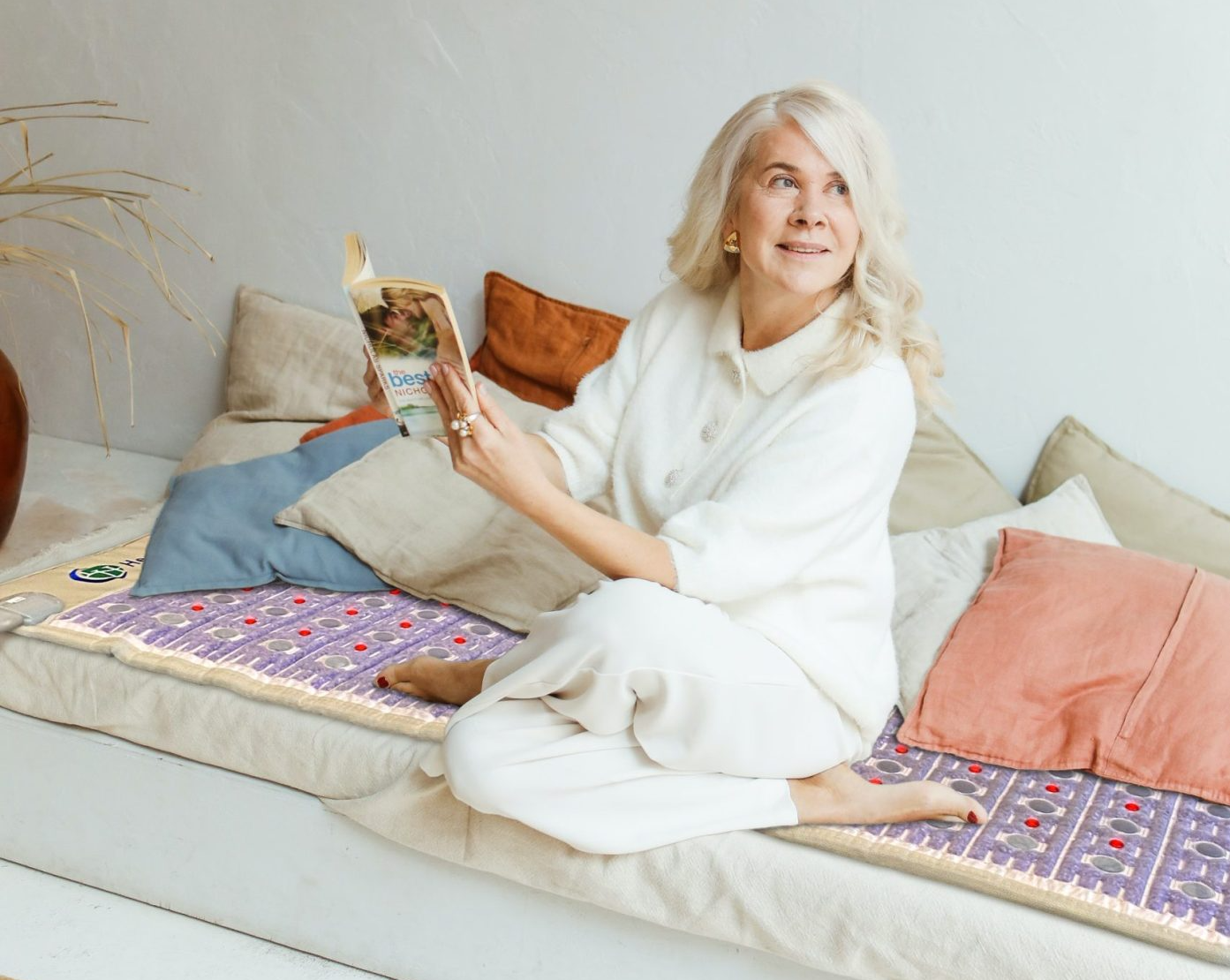 Woman sitting on a sofa using the HealthyLine TAJ PEMF mat for osteoarthritis joint pain relief. Woman sitting on a sofa using the HealthyLine TAJ PEMF mat for osteoarthritis joint pain relief.