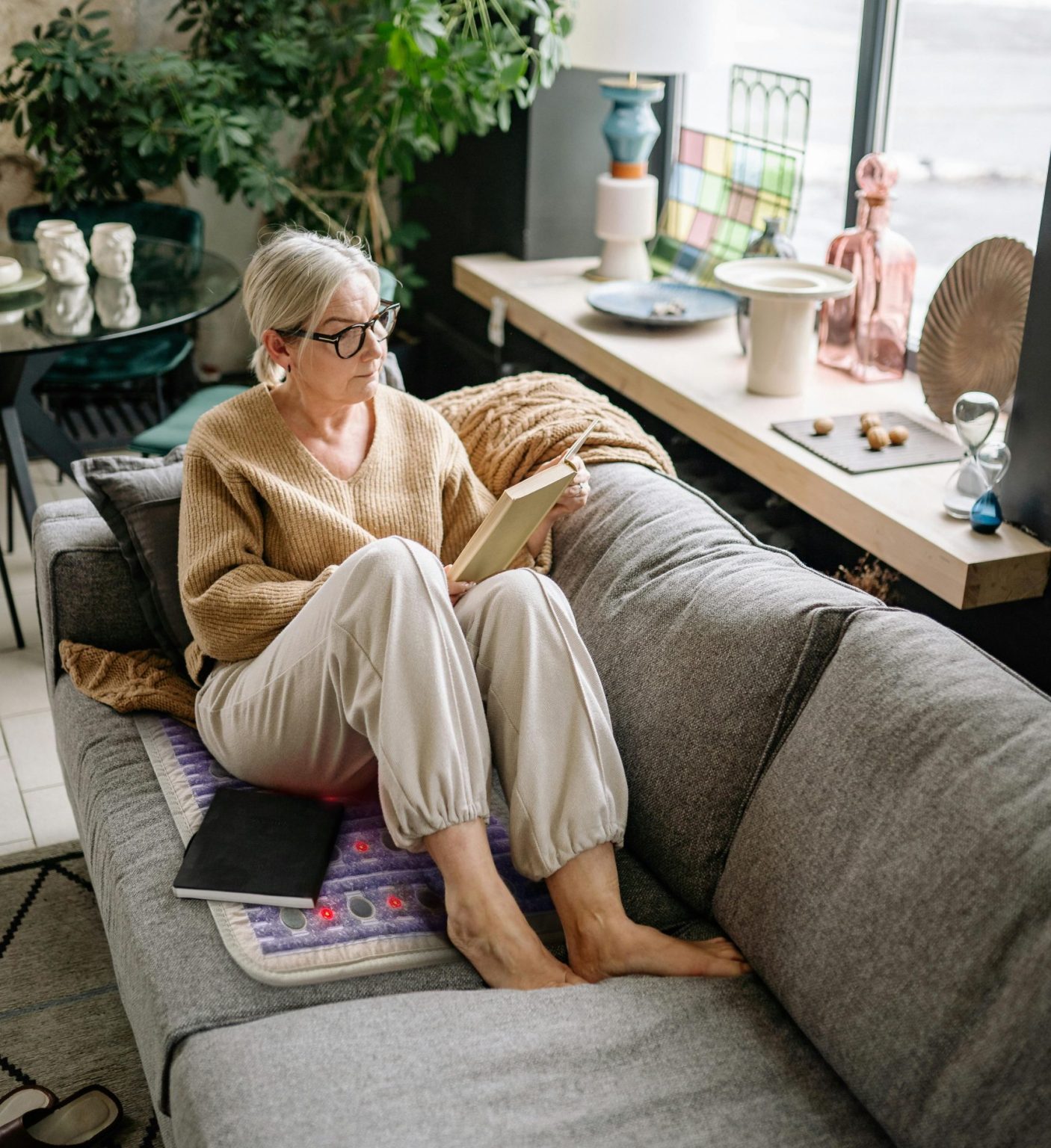 Elderly woman with osteoarthritis sitting on a sofa using the HealthyLine TAJ short PEMF mat for joint pain relief. Elderly woman with osteoarthritis sitting on a sofa using the HealthyLine TAJ short PEMF mat for joint pain relief.