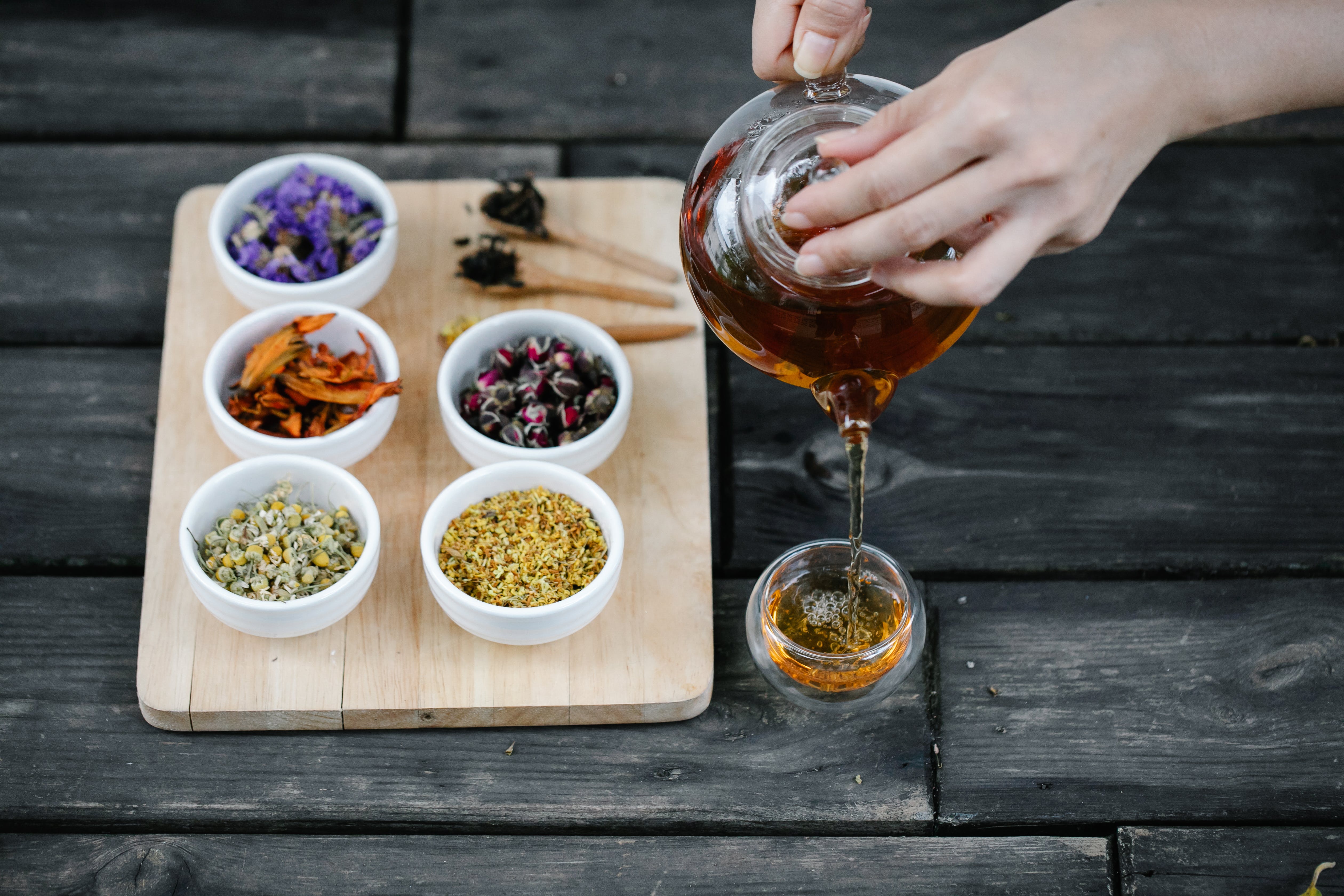 A steaming cup of herbal tea surrounded by dried nettle, lemon balm, and elderflower herbs, representing the Herbal Hydration Blend for sauna hydration.