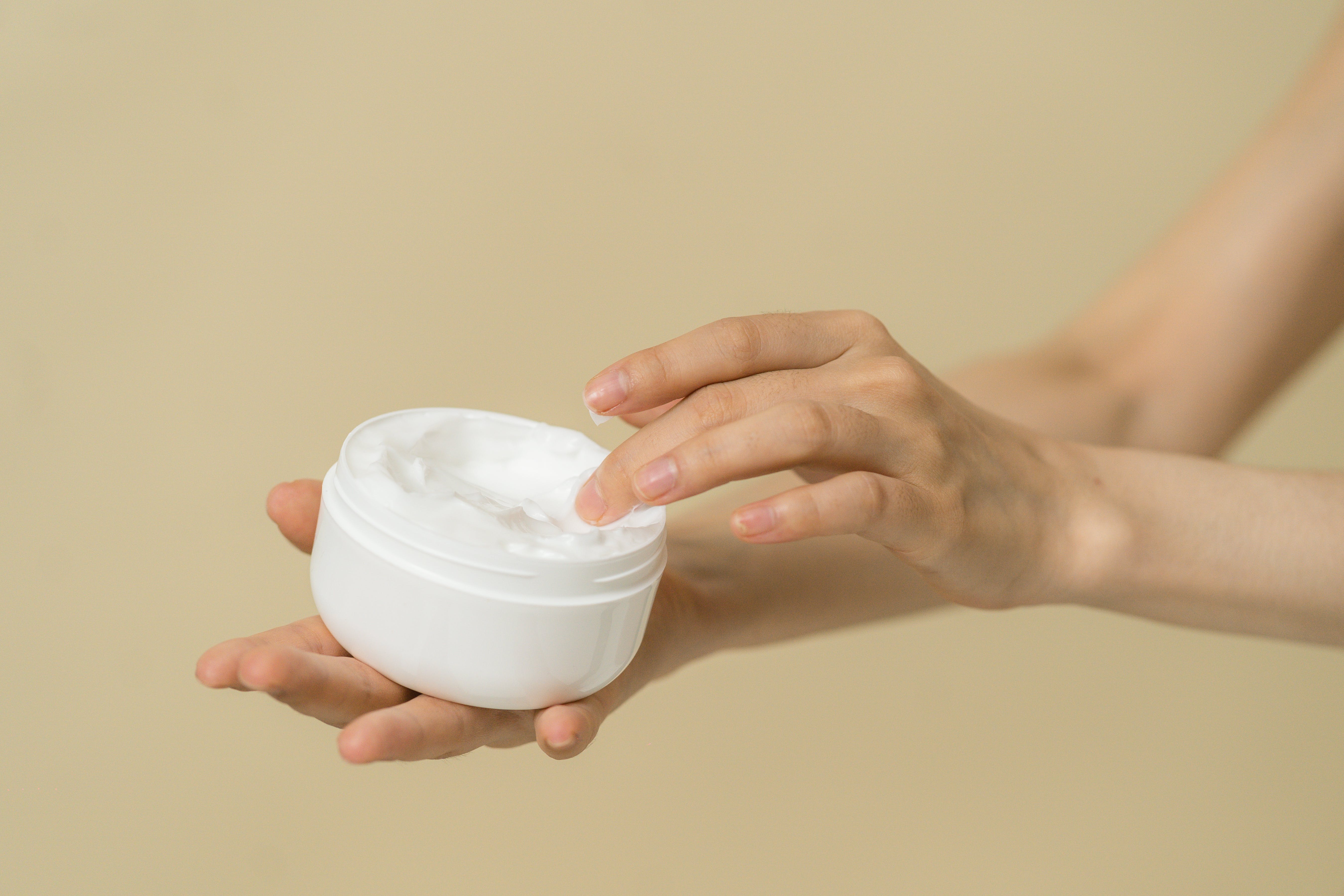 Hand applying cream from a pot, illustrating skincare for infrared sauna use Hand applying cream from a pot, illustrating skincare for infrared sauna use