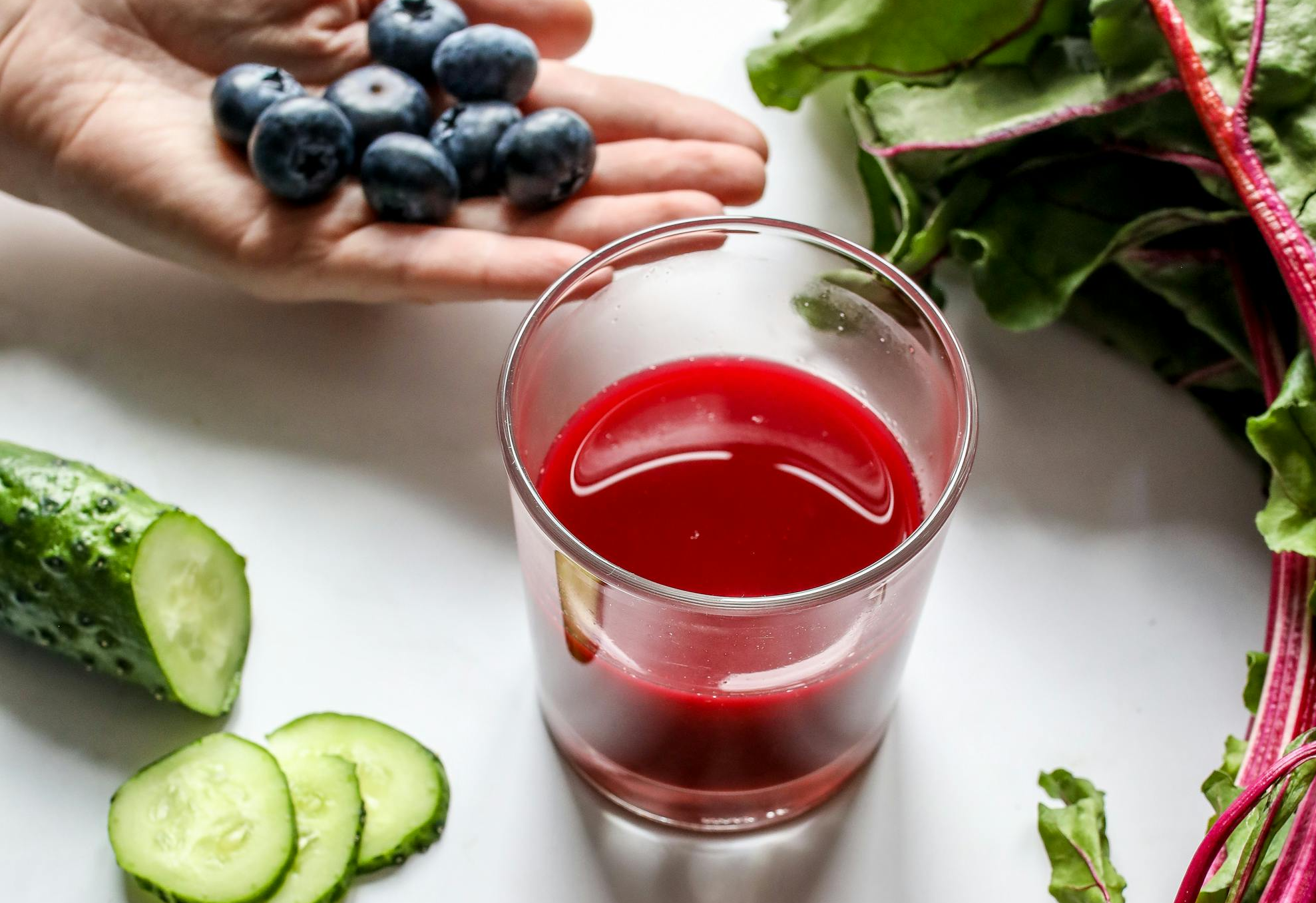 A glass filled with berry cucumber splash water, showing sliced cucumbers, strawberries, raspberries, and blueberries, chilled for hydration during sauna use.