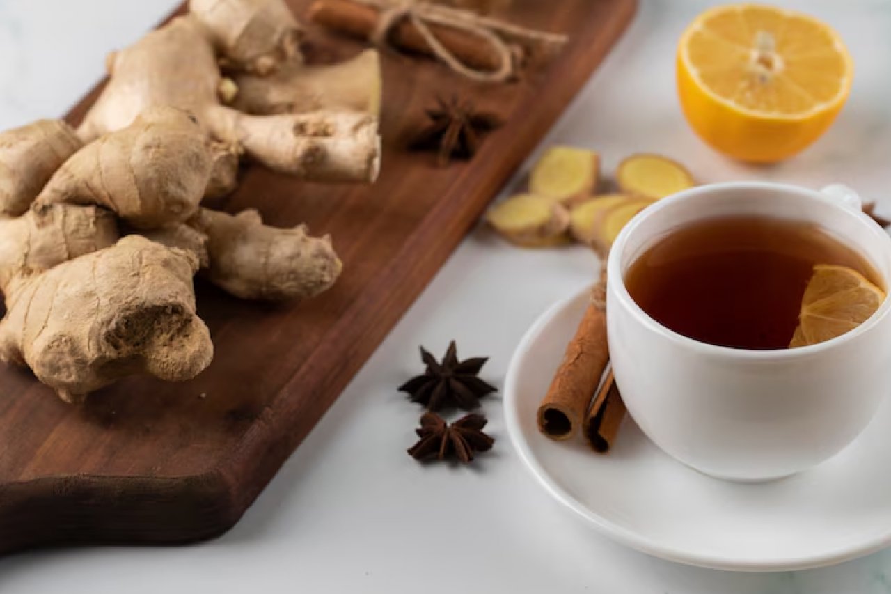 A cup of golden turmeric tea with a bright yellow color, garnished with a slice of lemon and a sprinkle of black pepper, placed on a wooden surface with fresh turmeric root nearby.
