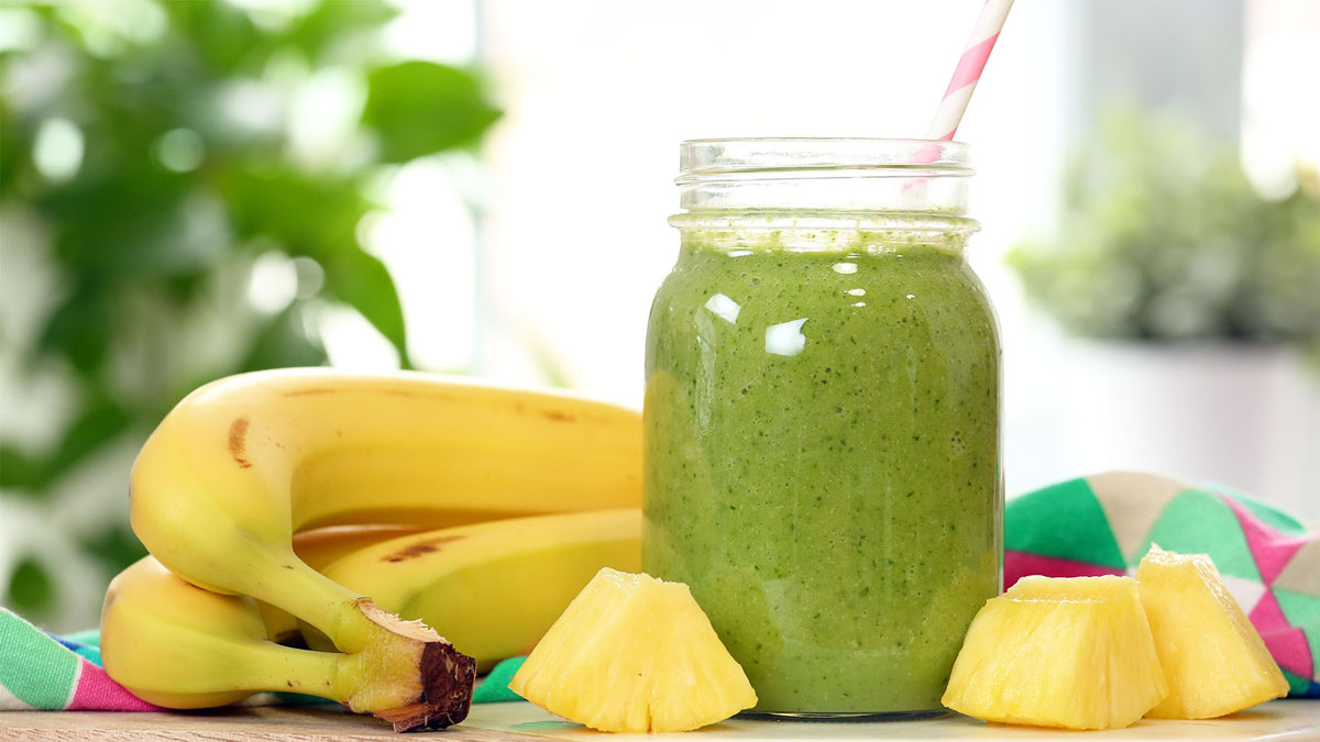 Tropical Recovery smoothie in a glass, blended with kale or spinach, pineapple, banana, cucumber, protein powder, peanut butter, and coconut water.