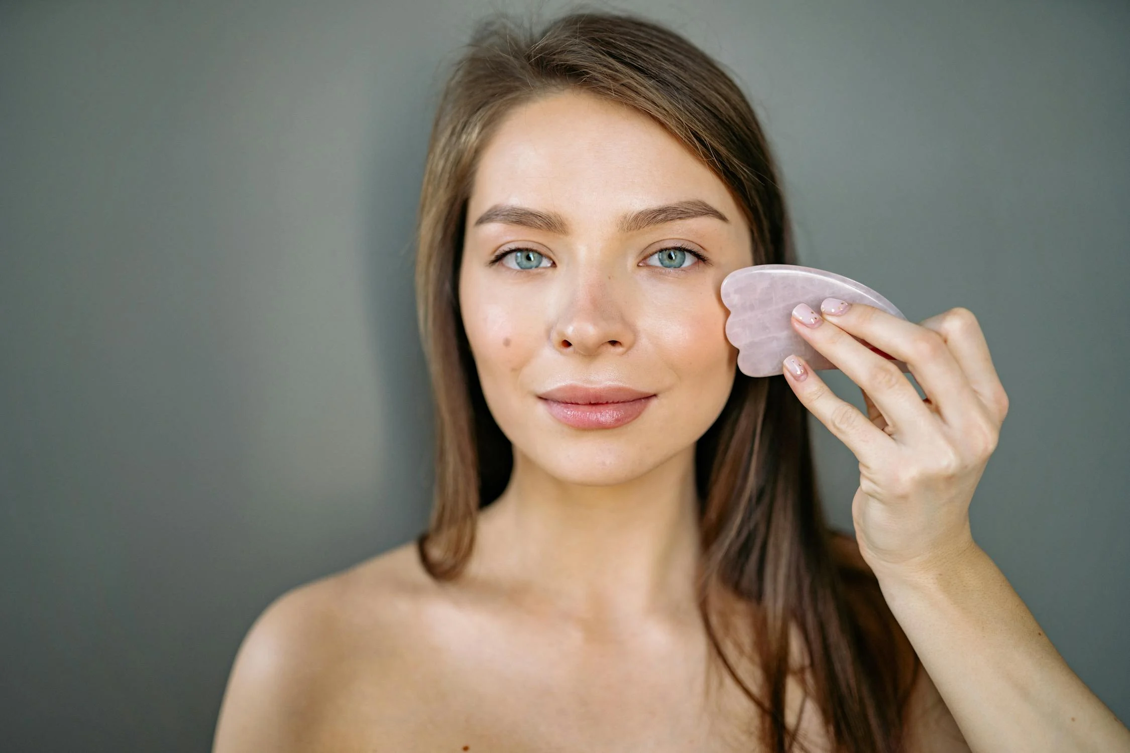 Woman using a Gua Sha tool for dry brushing as part of her skin care routine before a sauna session.